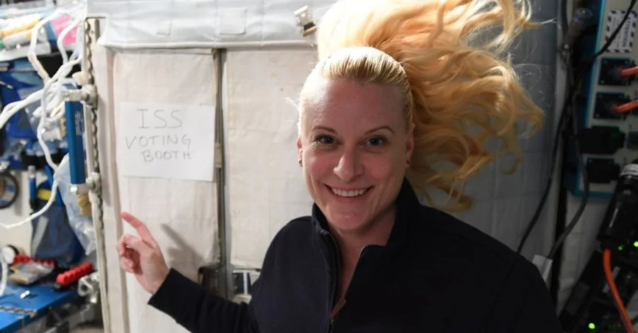 Kate Rubins aponta para a cabine de votação improvisada na Estação Espacial Internacional.