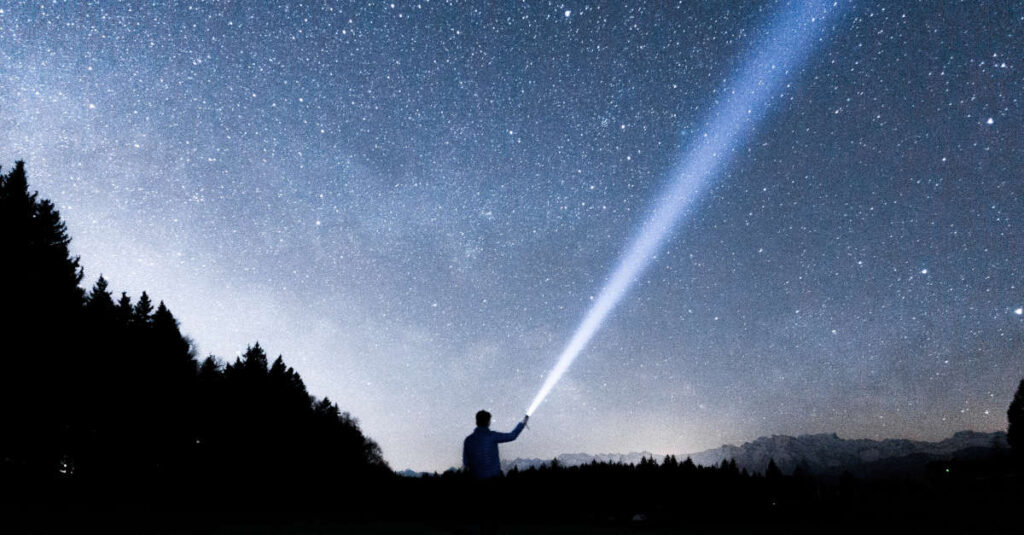 Homem aponta lanterna para o céu noturno. Imagem: Unsplash/Reprodução