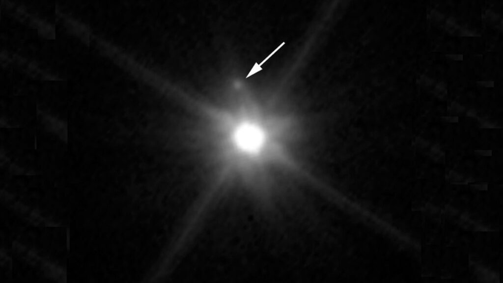 Makemake fotografado pelo Telescópio Espacial Hubble. A seta indica a pequena lua recém-descoberta ao redor do planeta anão. Imagem: NASA, ESA e A. Parker e M. Buie (SwRI)