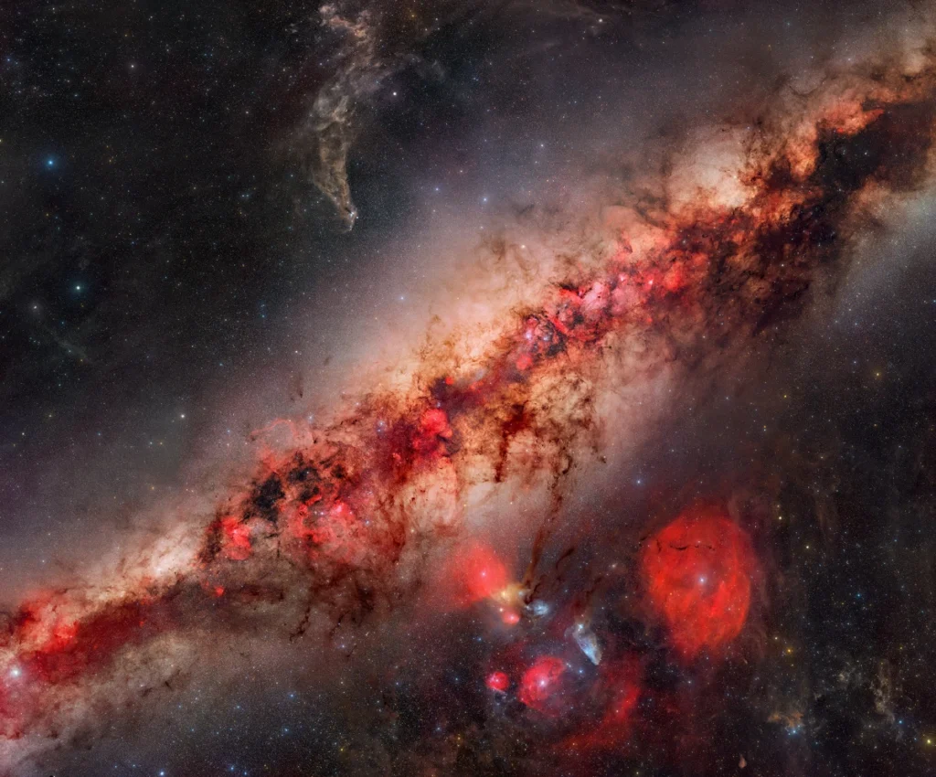 Um olhar profundo para o núcleo da Via Láctea © Jakob Sahner (Alemanha). Este mosaico da Via Láctea foi capturado com o uso de duas câmeras: uma para cor RGB e outra para H-alfa, a fim de registrar o máximo possível de detalhes e estruturas. O projeto quase desmoronou quando anéis de Newton inesperados, um fenômeno óptico que pode ocorrer ao trabalhar com filtros, apareceram em muitos dos painéis após o empilhamento. Jakob Sahner considerou abandonar todo o conjunto de dados, mas acabou encontrando uma forma de corrigir a maior parte dele e preservar a imagem. No fim, o resultado foi um mosaico de aproximadamente 750 megapixels. Capturada com câmeras Sony Alpha 7 III e Nikon Z 6, lente Samyang 135 mm f/2, montagem Sky-Watcher Star Adventurer GTi, 135 mm f/2, ISO 1600, 1.950 exposições H-alfa de 90 segundos, 2.182 exposições RGB de 90 segundos. Local: Koireb, Windhoek Rural, Namíbia, 19 de maio a 1º de junho de 2025
