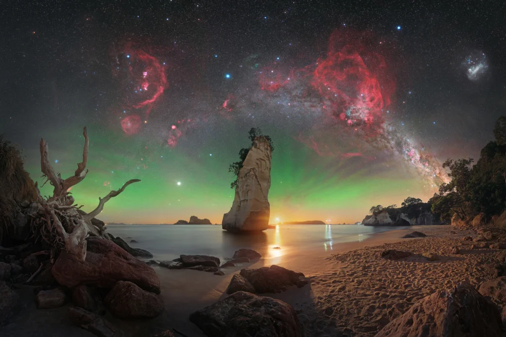 Nascer da Lua em Te Hoho Rock © Evan McKay (Aotearoa/Nova Zelândia). Naquela noite em particular, Evan McKay tinha apenas uma pequena janela para capturar o céu antes que a Lua começasse a nascer. McKay alinhou sua montagem polar durante o crepúsculo e então começou a fotografar o panorama do céu a partir daquele local. A luz da Lua ofereceu o melhor dos dois mundos e iluminou o primeiro plano de maneira fantástica. Para realçar o céu, McKay capturou um panorama separado usando um filtro duplo de banda estreita e o combinou à imagem para destacar as nebulosas. Capturada com uma câmera Nikon Z 6a, montagem Sky-Watcher EQ6-R Pro, rastreador estelar Move Shoot Move Nomad, lente Sigma 40 mm Art, filtro Optolong L-Para, 40 mm. Primeiro plano: f/2.8, ISO 800, exposição de 30 segundos; céu: f/2, ISO 1600, múltiplas exposições RGB de 15 segundos, múltiplas exposições de 2 minutos com filtro. Local: Cathedral Cove, Waikato, Ilha Norte, Aotearoa/Nova Zelândia, 8 de janeiro de 2026