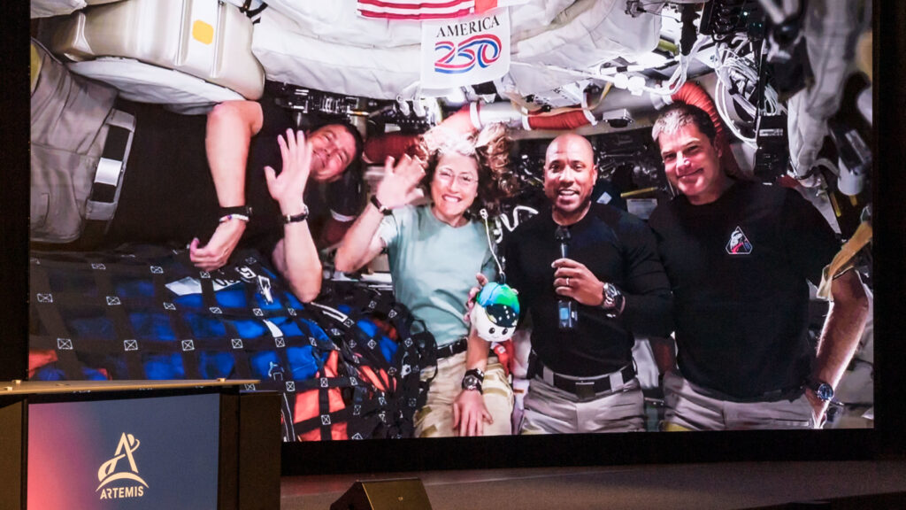 Foto de uma transmissão ao vivo do espaço em que a imprensa nos EUA se reuniu para fazer perguntas à tripulação da Artemis II durante seu retorno à Terra. 