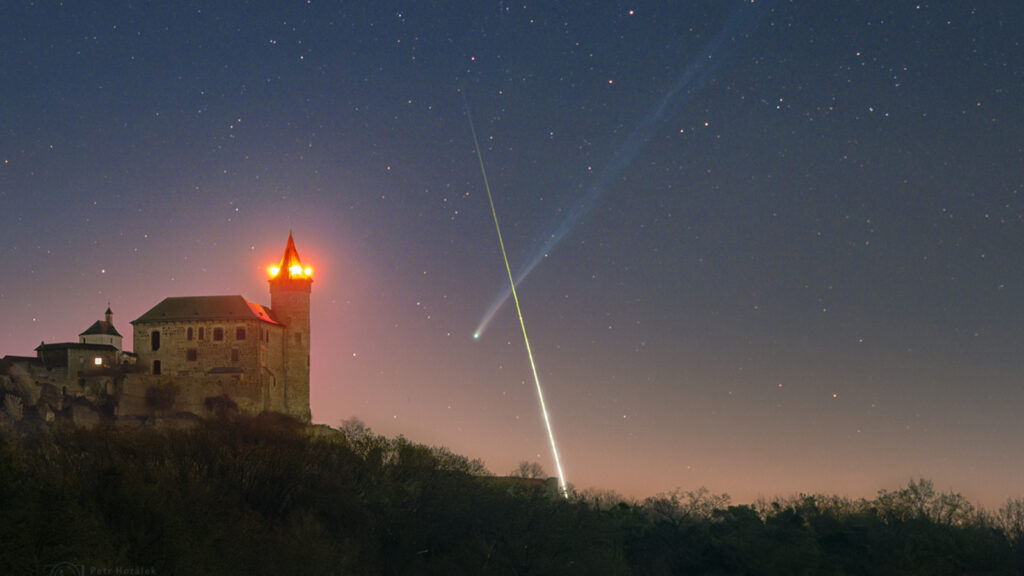 Um brilhante meteoro passa na frente da longa cauda do cometa C/2025 R3 (PanSTARRS) sobre um castelo checo na madrugada de 18 de abril. 
